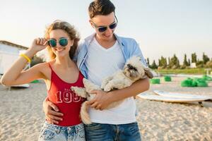 young attractive smiling couple having fun on beach playing with dogs photo