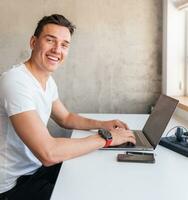 young handsome man in casual outfit sitting at table working on laptop, typing, freelancer at home photo