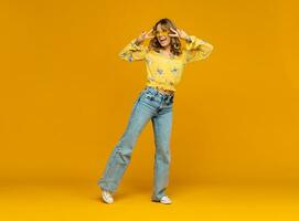 stylish happy smiling blond woman posing in jeans on yellow background photo