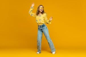 stylish happy smiling blond woman posing in jeans on yellow background photo