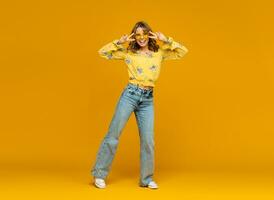 stylish happy smiling blond woman posing in jeans on yellow background photo