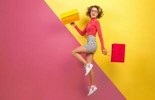 smiling attractive woman in stylish colorful outfit jumping with shopping bags photo