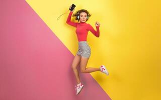 smiling attractive smiling excited woman in stylish colorful outfit jumping and listening to music photo