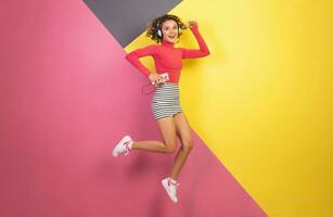 smiling attractive smiling excited woman in stylish colorful outfit jumping and listening to music photo