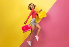 smiling attractive woman in stylish colorful outfit jumping with shopping bags photo