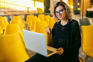 portrait of young attractive woman sitting in lecture hall working on laptop photo