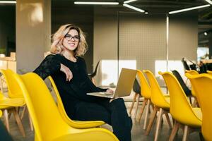 portrait of young attractive woman sitting in lecture hall working on laptop photo