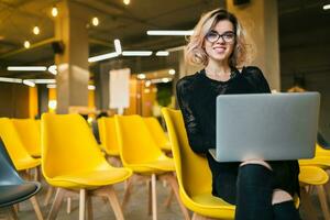 portrait of young attractive woman sitting in lecture hall working on laptop photo