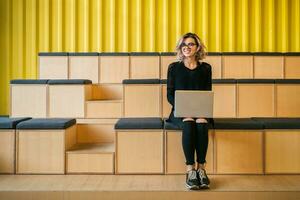 portrait of young attractive woman sitting in lecture hall working on laptop photo