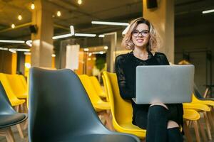 portrait of young attractive woman sitting in lecture hall working on laptop photo