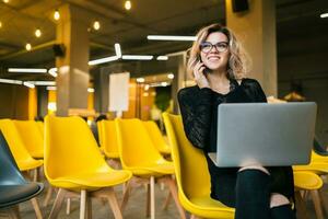 portrait of young attractive woman sitting in lecture hall working on laptop photo