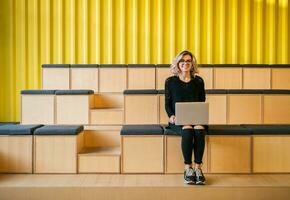 portrait of young attractive woman sitting in lecture hall working on laptop photo