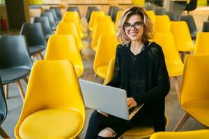 portrait of young attractive woman sitting in lecture hall working on laptop photo