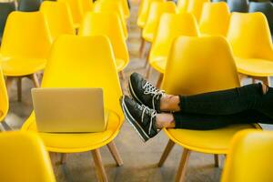 close up legs of young stylish woman sitting in lecture hall with laptop photo