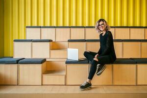 portrait of young attractive woman sitting in lecture hall working on laptop photo