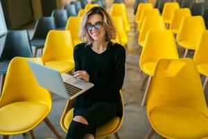 portrait of young attractive woman sitting in lecture hall working on laptop photo