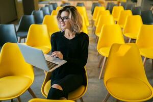 portrait of young attractive woman sitting in lecture hall working on laptop photo