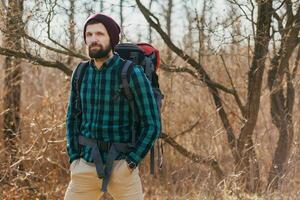 young hipster man traveling with backpack in spring autumn forest photo