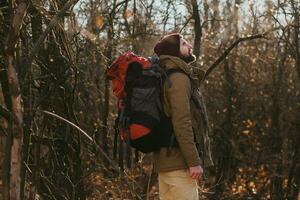 young hipster man traveling with backpack in spring autumn forest photo
