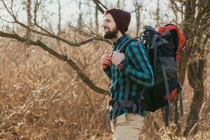 young hipster man traveling with backpack in spring autumn forest photo