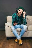 young hipster handsome bearded man sitting on a couch at home, listening to music photo