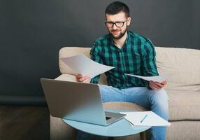 young hipster handsome bearded man sitting on couch at home photo