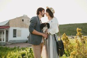 young stylish hipster couple in love walking with dog in countryside, having fun photo