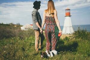 view from back on young stylish hipster couple in love walking with dog in countryside photo