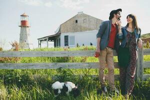 young stylish hipster couple in love walking with dog in countryside, summer style boho fashion photo