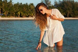 slim beautiful woman in white cotton dress walking on tropical beach photo