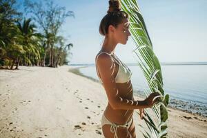 joven flaco mujer en blanco bikini trajes de baño participación hoja de palma árbol foto