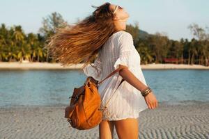 slim beautiful woman in white cotton dress walking on tropical beach photo