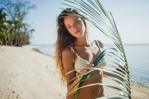 joven flaco mujer en blanco bikini trajes de baño participación hoja de palma árbol foto