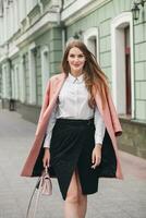 young stylish beautiful woman walking in street, wearing pink coat photo