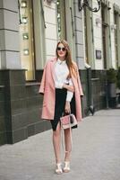 young stylish beautiful woman walking in street, wearing pink coat photo