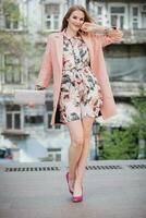 portrait of attractive stylish smiling woman walking city street in pink coat photo