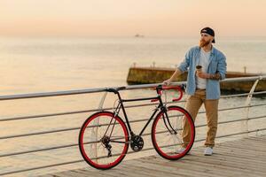 handsome bearded man traveling with bicycle in morning sunrise by the sea photo