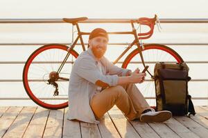 handsome bearded man traveling with bicycle in morning sunrise using phone photo