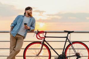 young bearded man traveling on bicycle at sunset sea photo