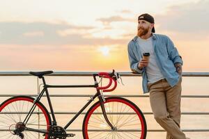young bearded man traveling on bicycle at sunset sea photo