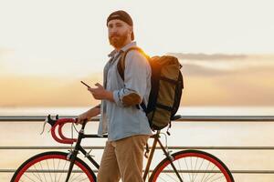 handsome bearded man traveling with bicycle in morning sunrise by the sea photo