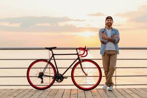 joven barbado hombre de viaje en bicicleta a puesta de sol mar foto