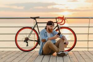 young bearded man traveling on bicycle at sunset sea photo