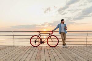 joven barbado hombre de viaje en bicicleta a puesta de sol mar foto