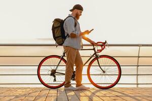 young bearded man traveling on bicycle at sunset sea photo