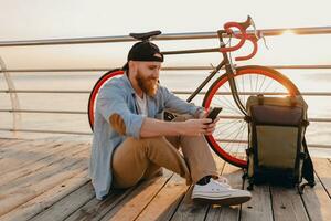 young bearded man traveling on bicycle at sunset sea photo