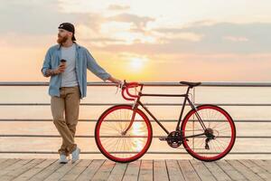 joven barbado hombre de viaje en bicicleta a puesta de sol mar foto