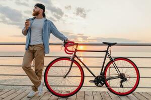 handsome bearded man traveling with bicycle in morning sunrise by the sea photo