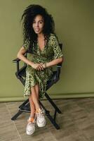 attractive black african american woman posing in stylish green dress isolated on green background photo