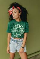 attractive black african american woman posing in stylish hipster outfit on green background photo